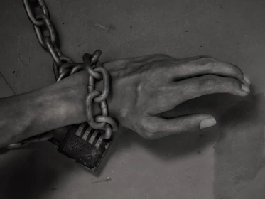 Close-up of hands breaking free from chains under a bright light.