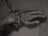 A human hand is bound by thick, heavy chains, which are fastened with a lock. The lighting and shadows cast a gloomy and somber atmosphere.
