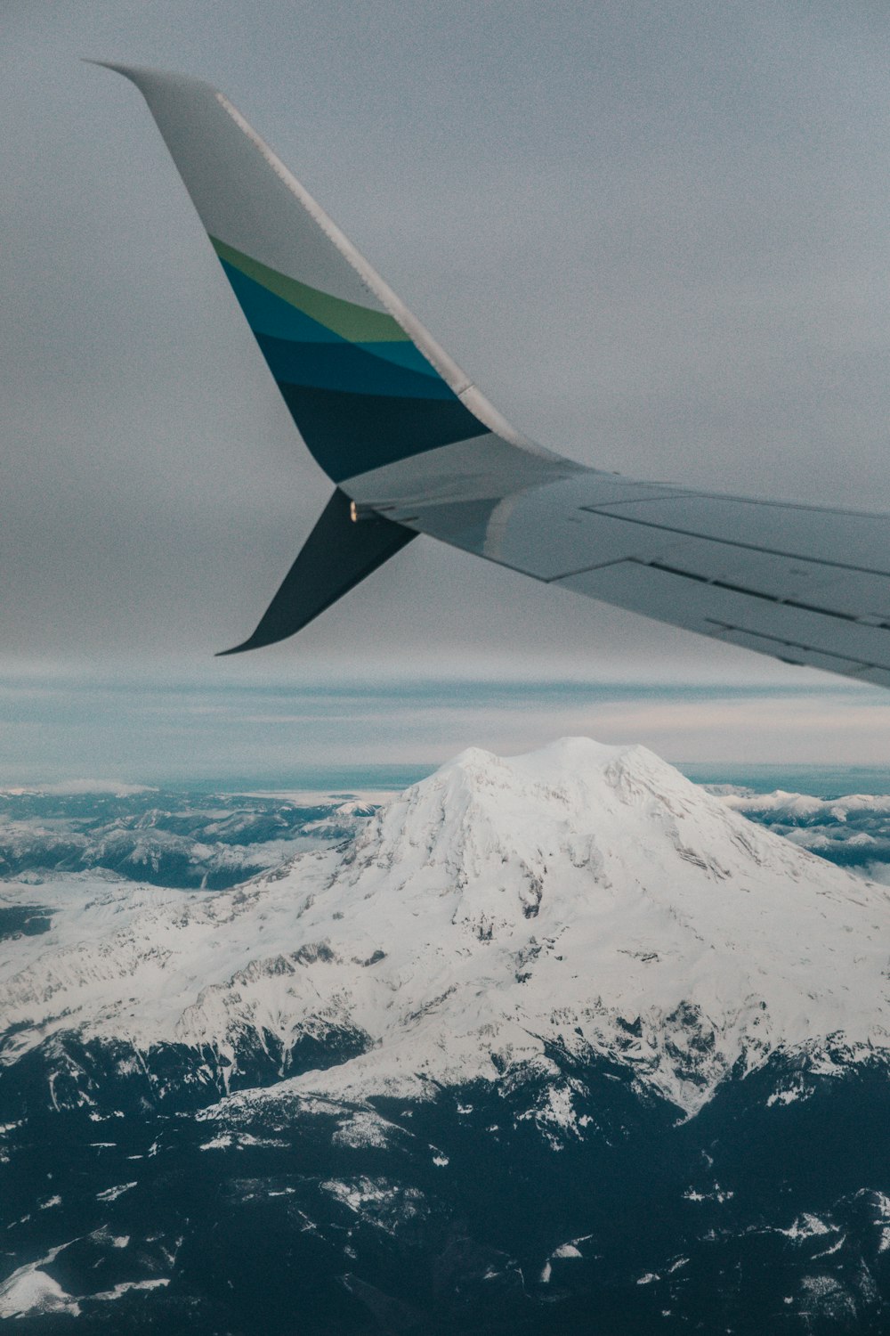 an airplane wing flying over a snow covered mountain