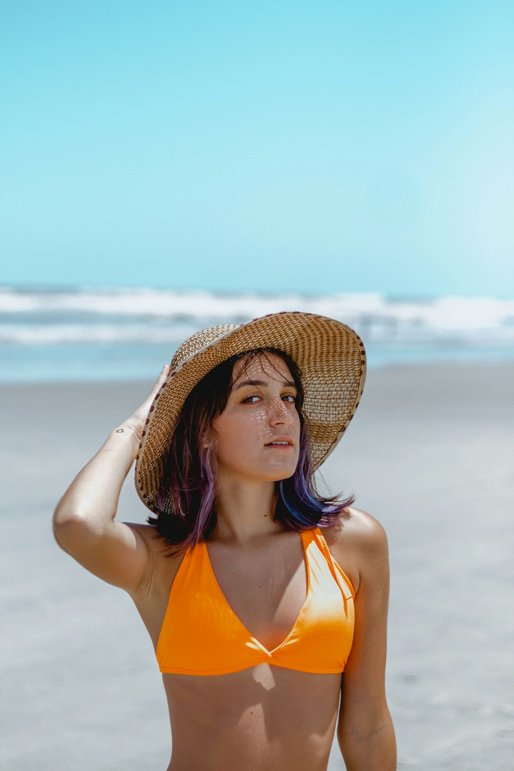 woman in orange bikini wearing brown sun hat standing on beach during daytime