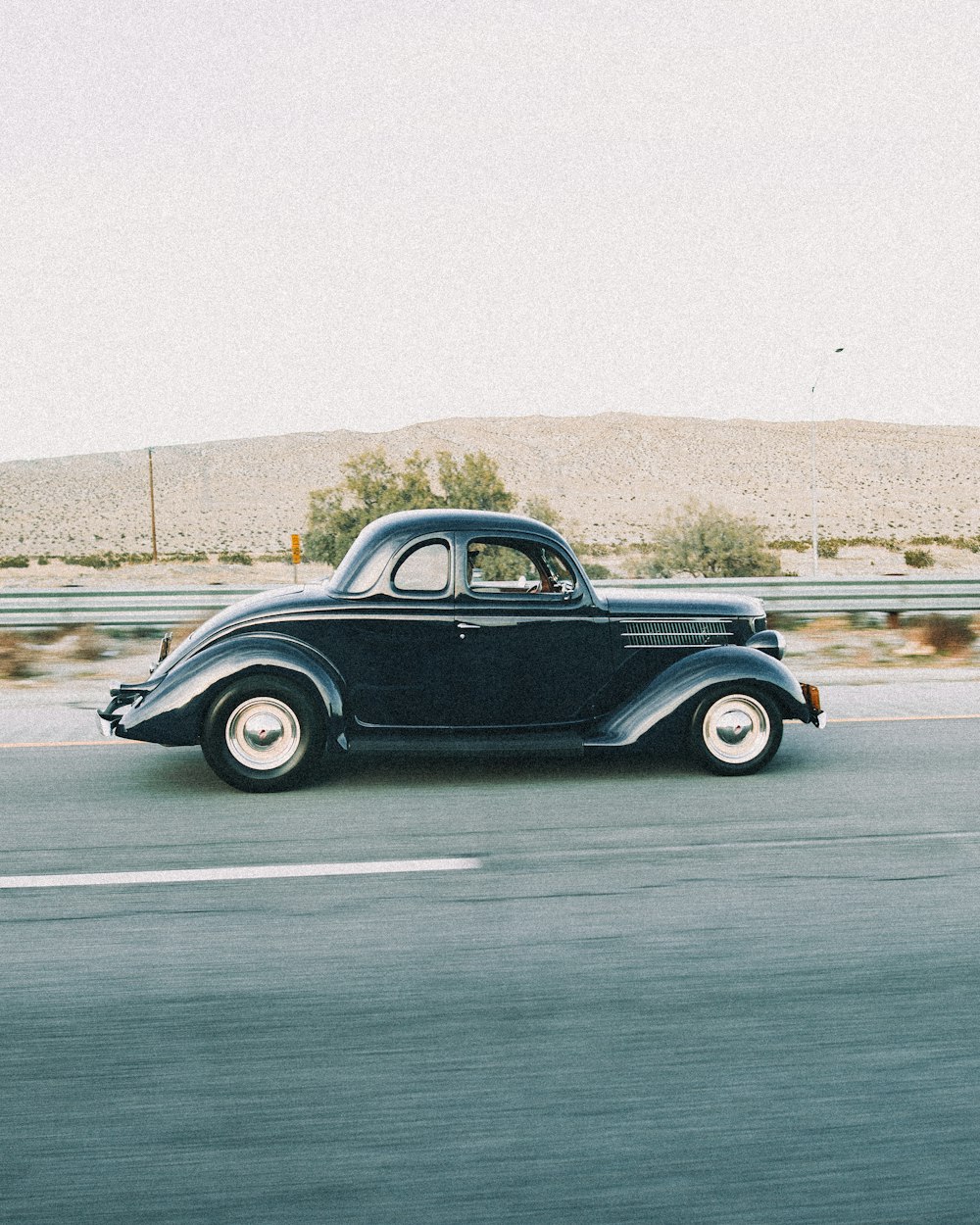 an old black car driving down the road