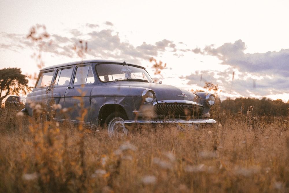 an old car parked in a field of tall grass