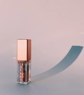 Glossy lip gloss tube reflecting soft sunlight on a wooden table