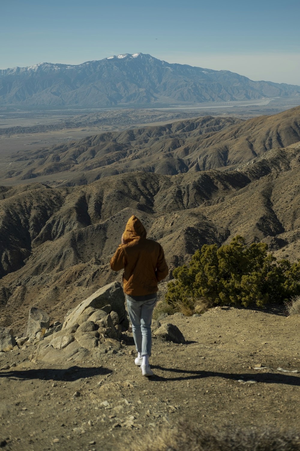 woman in brown jacket and white pants standing on rocky mountain during daytime
