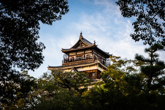 brown and white pagoda temple surrounded by green trees under white clouds and blue sky during in Hiroshima Castle Japan