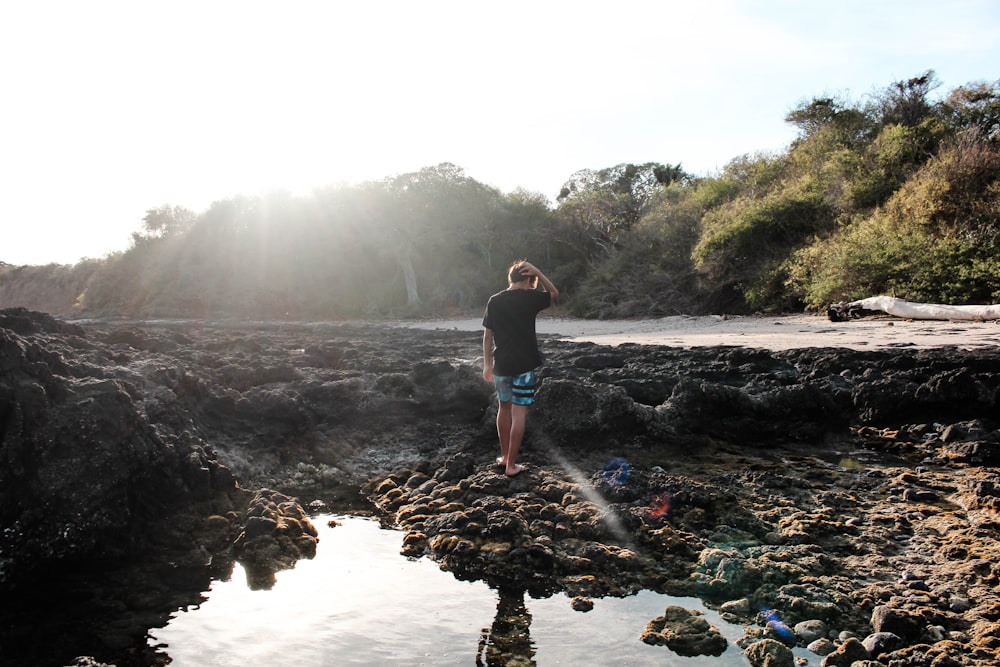 woman in black tank top and blue denim shorts standing on rocky shore during daytime