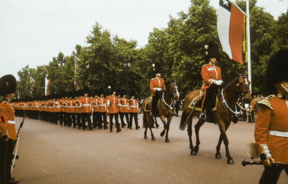 persone in uniforme rossa e nera che cavalcano cavalli durante il giorno