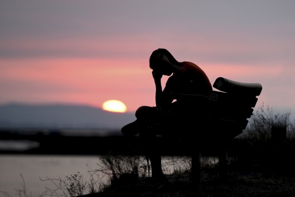 silhouette of woman sitting on bench during sunset