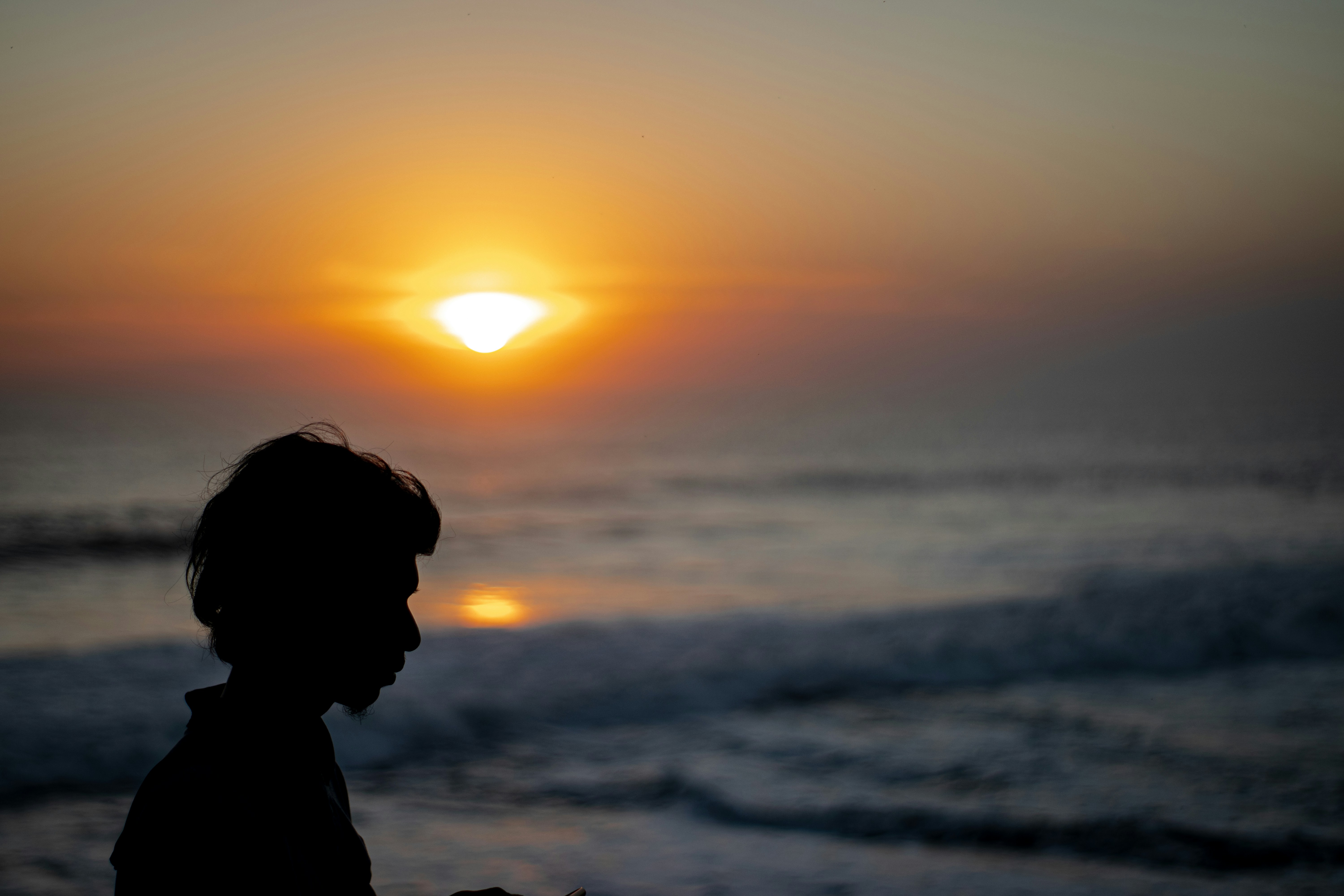 silhouette of man standing near sea during sunset