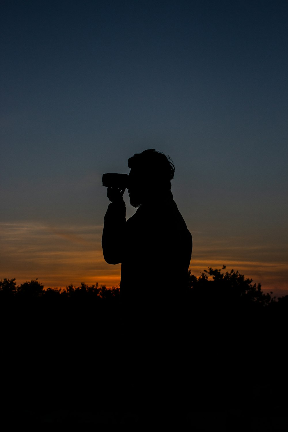 silhouette of man holding camera during sunset