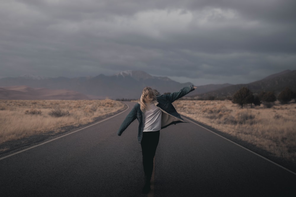 woman in gray long sleeve shirt and black pants standing on black asphalt road during daytime