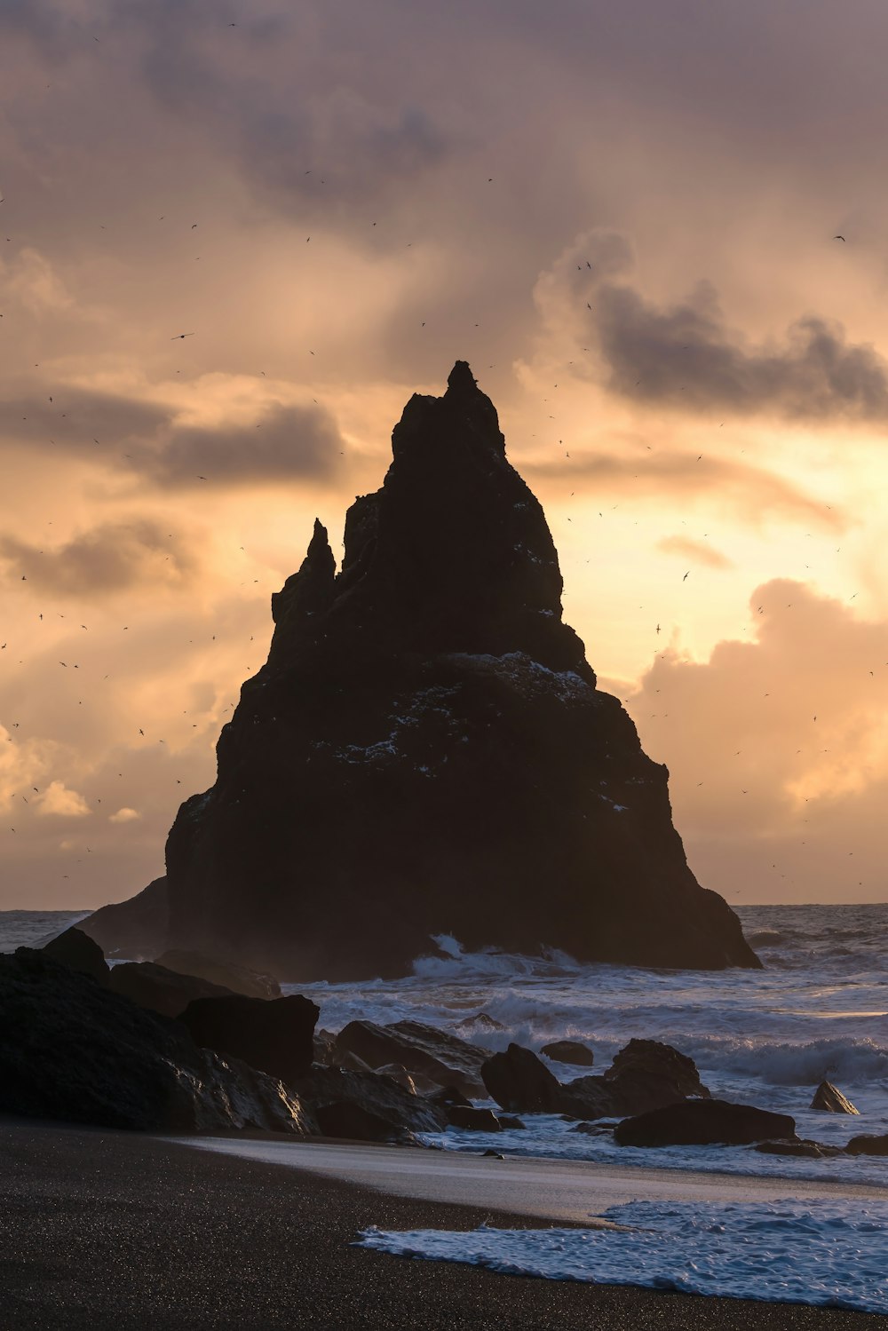 silhouette of rock formation on sea during sunset