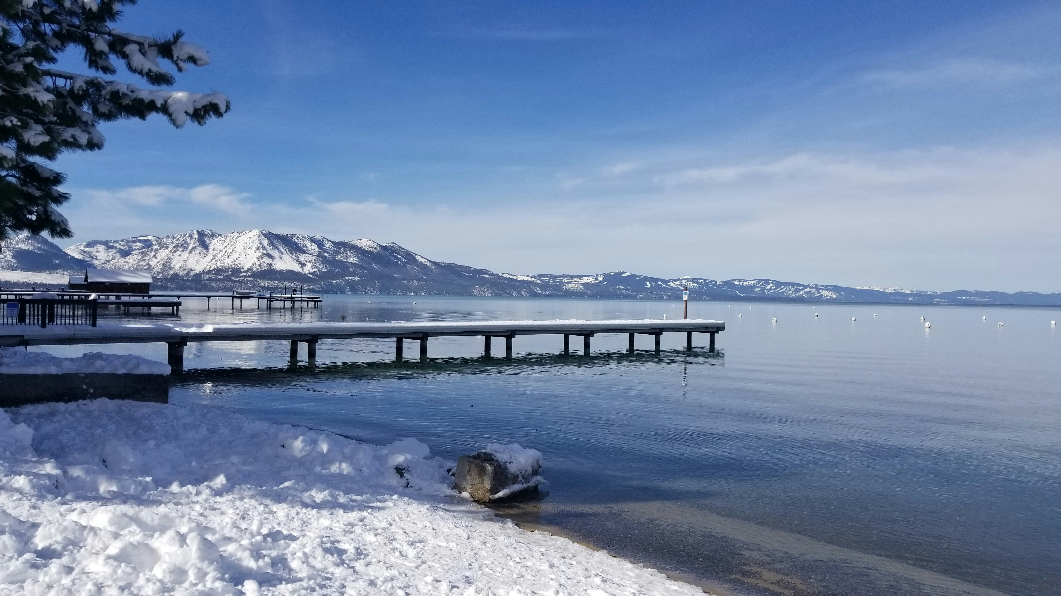muelle de madera marrón en el lago cerca de la montaña cubierta de nieve bajo el cielo azul durante el día