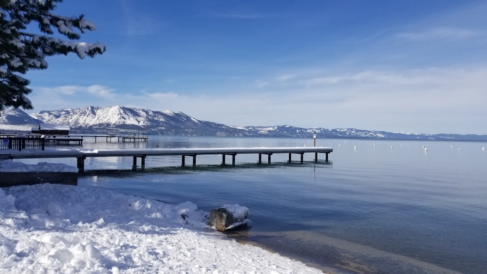 brown wooden dock on lake near snow covered mountain under blue sky during daytime