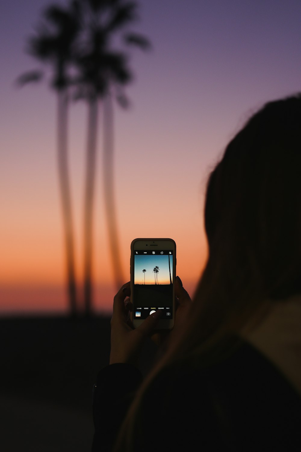 person holding iphone taking photo of sunset