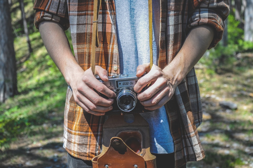 man in brown and black plaid button up shirt holding black and silver camera
