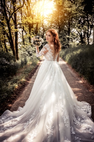 woman in white floral dress standing on brown soil surrounded by green plants and trees during