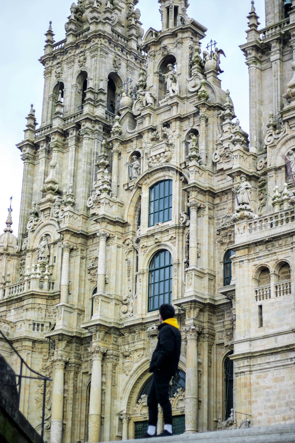 낮에 갈색 콘크리트 건물 앞에 서 있는 검은 재킷을 입은 남자