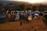 A series of padlocks are attached to a metal cable against the backdrop of a sunset. The locks vary in size, shape, and color, including a combination lock. The background is blurred, emphasizing the locks in the foreground.