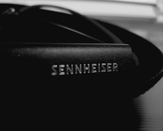A close-up of a Sennheiser branded audio equipment part, likely headphones or a microphone, with a focus on the logo in white on a black surface.