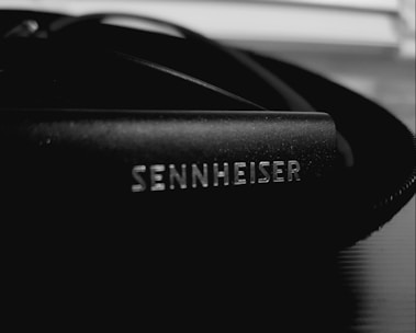 A close-up of a Sennheiser branded audio equipment part, likely headphones or a microphone, with a focus on the logo in white on a black surface.
