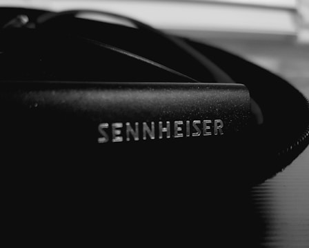 A close-up of a Sennheiser branded audio equipment part, likely headphones or a microphone, with a focus on the logo in white on a black surface.