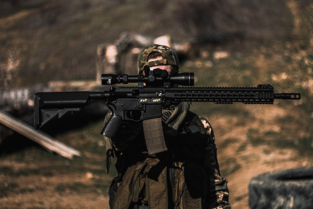 homme en veste de camouflage noire et marron tenant un fusil d’assaut noir