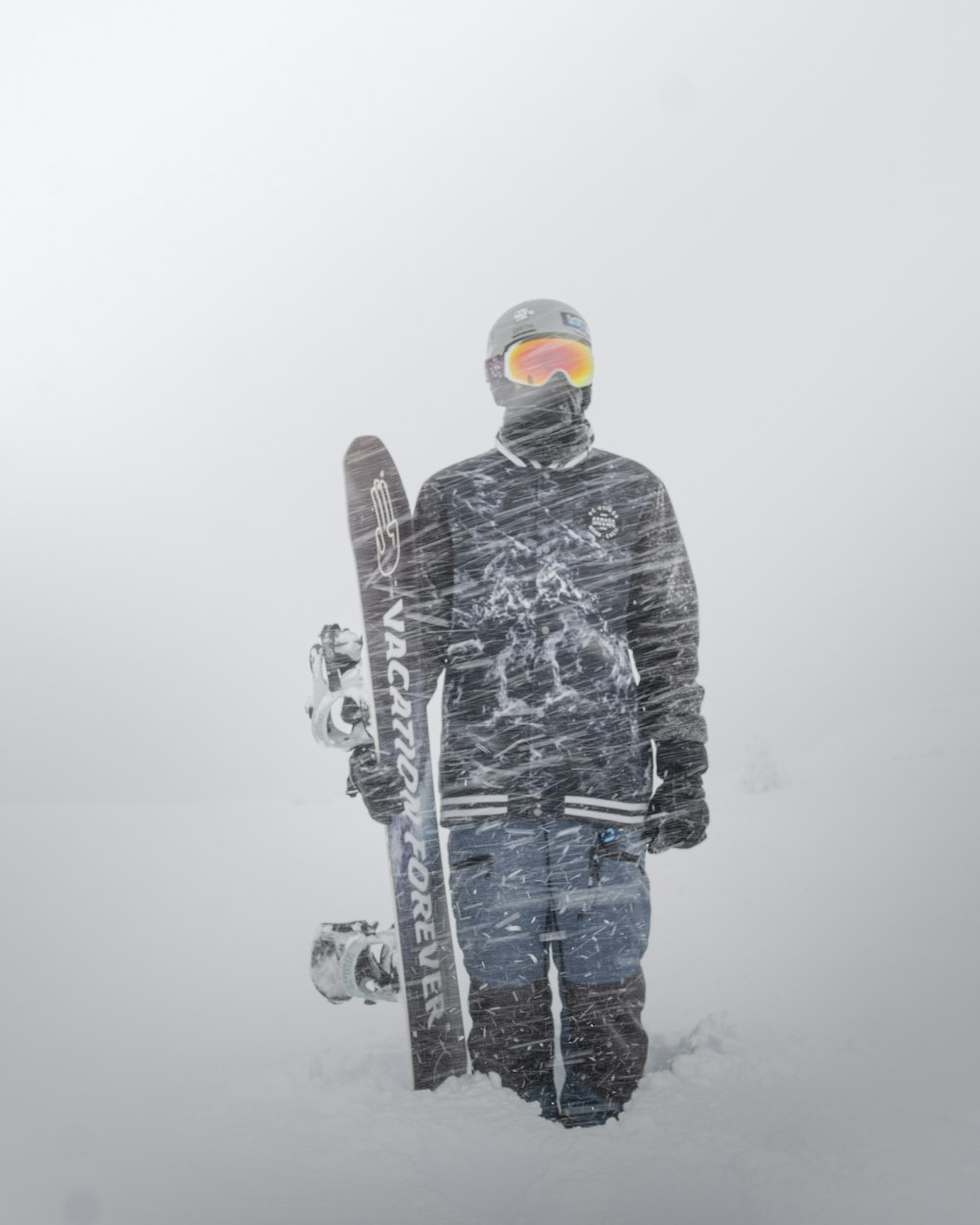 man in black and gray jacket and blue pants holding white and red snowboard