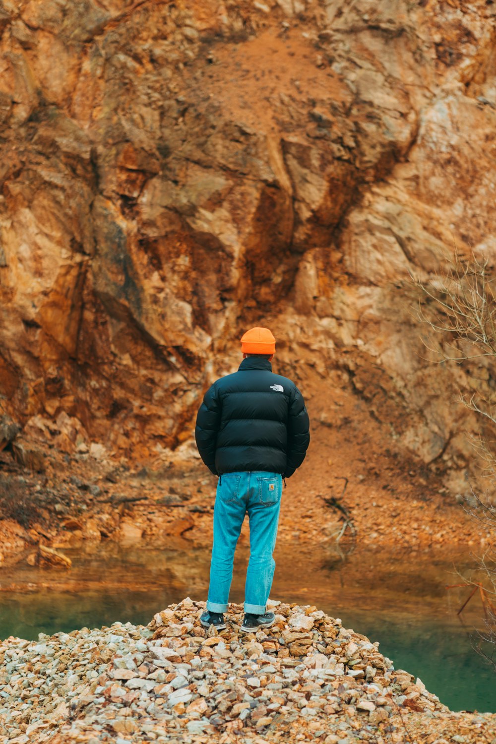 homem em jaqueta preta e jeans azuis em pé na formação rochosa marrom durante o dia