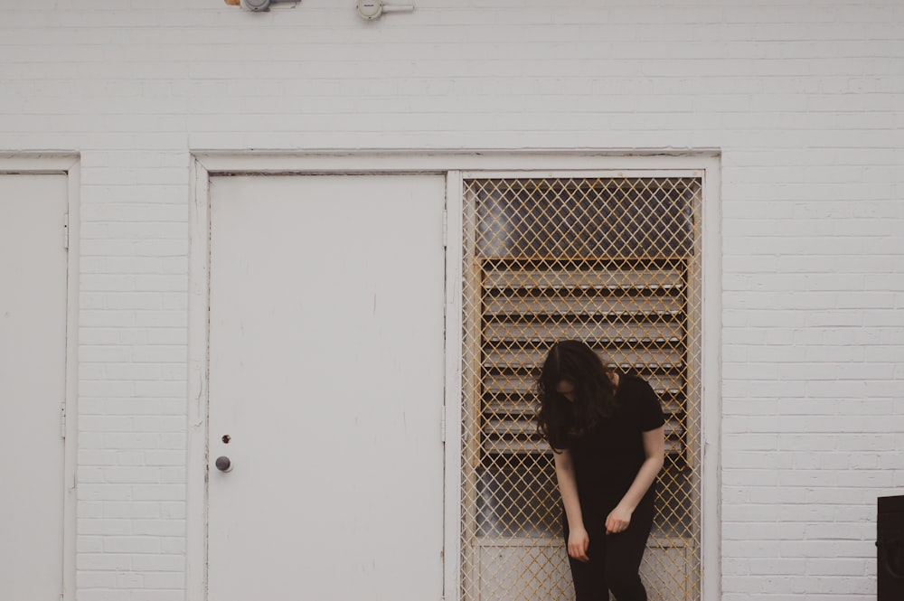 mujer en vestido negro apoyada en puerta de madera blanca