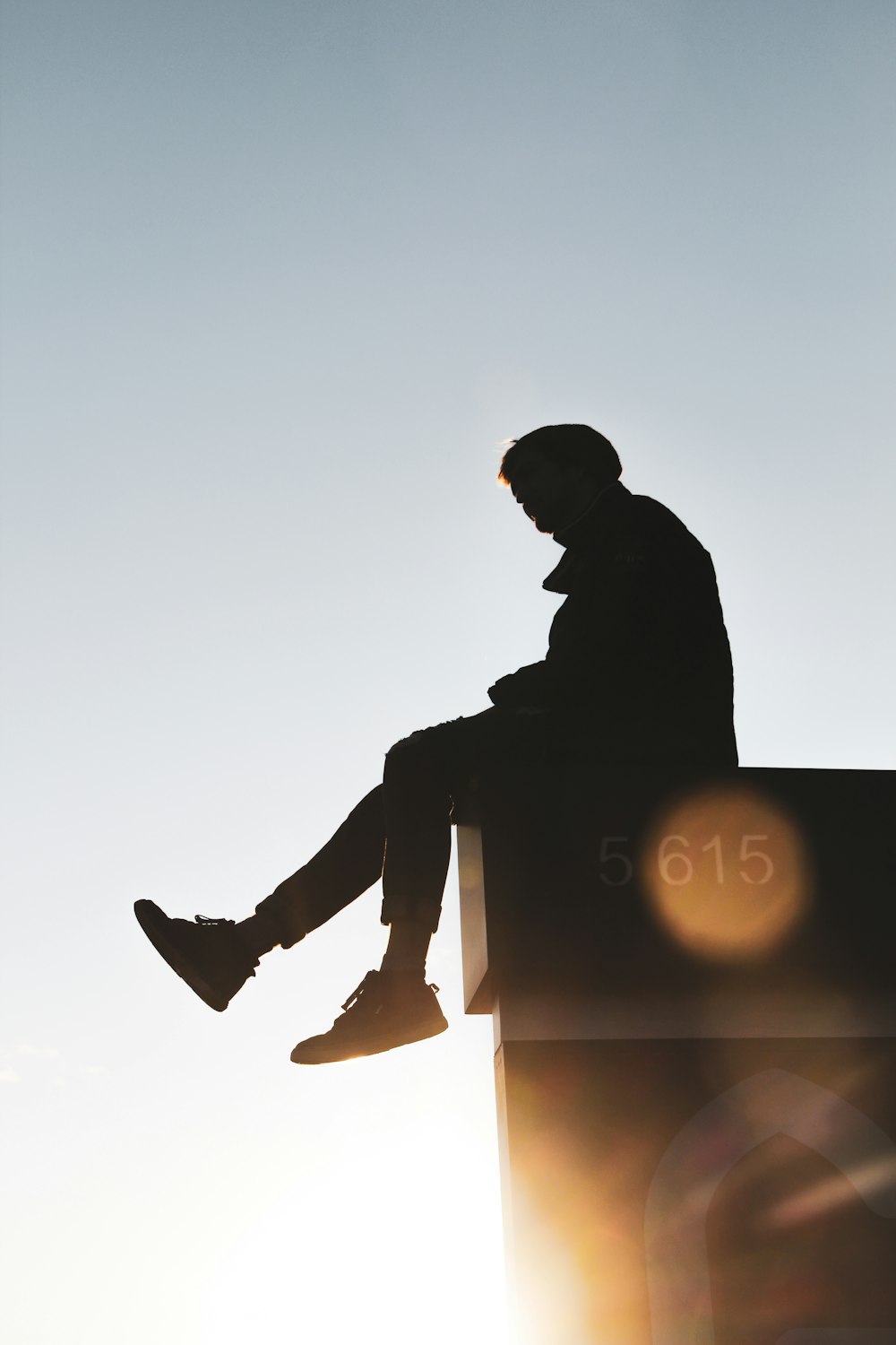 silhouette of man sitting on the edge of the building during sunset