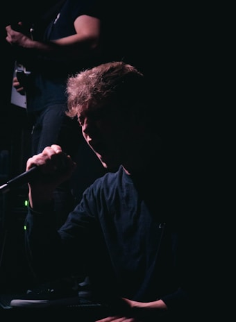 Hervé Dipari performing on stage with microphone in hand, spotlight highlighting his expressive face.