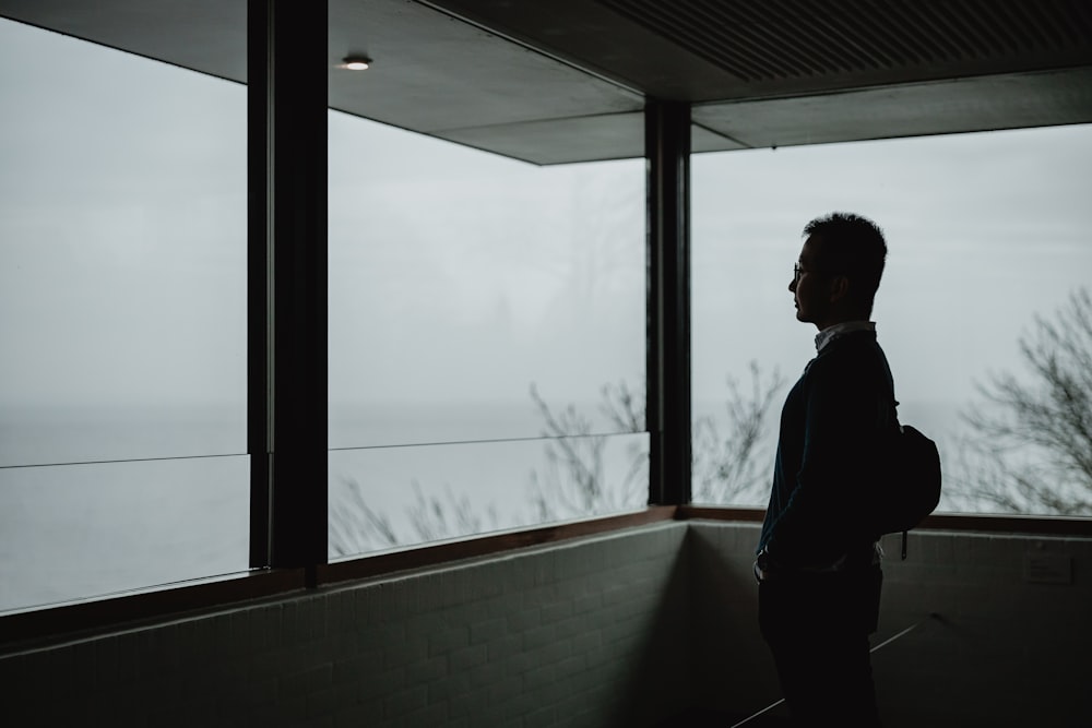 man in blue jacket standing beside window