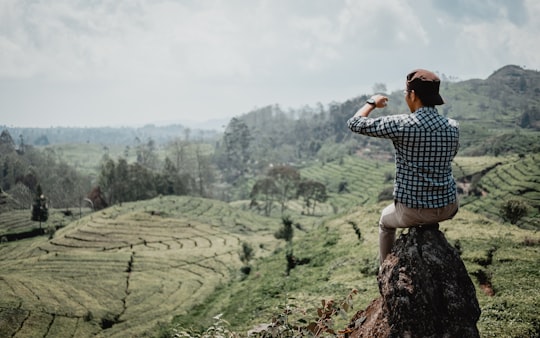 man in blue and white checkered dress shirt standing on green grass field during daytime in Bandung Indonesia