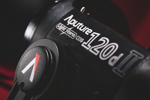Close-up view of a professional studio light labeled 'Aputure 120d II' with a black cylindrical body and control knob featuring a logo.