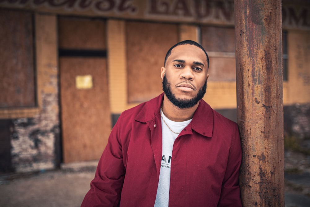 man in red zip up jacket standing near brown wooden post during daytime