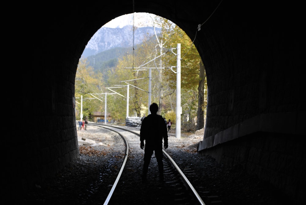 man in black jacket walking on train rail during daytime