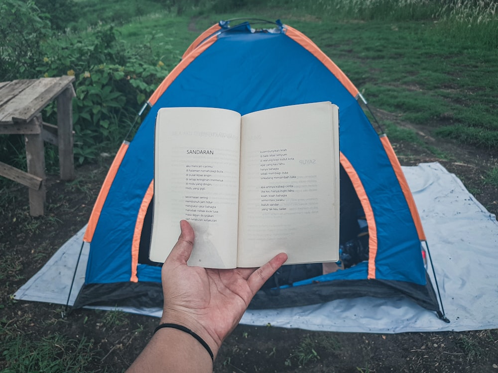 person holding book in blue and orange dome tent