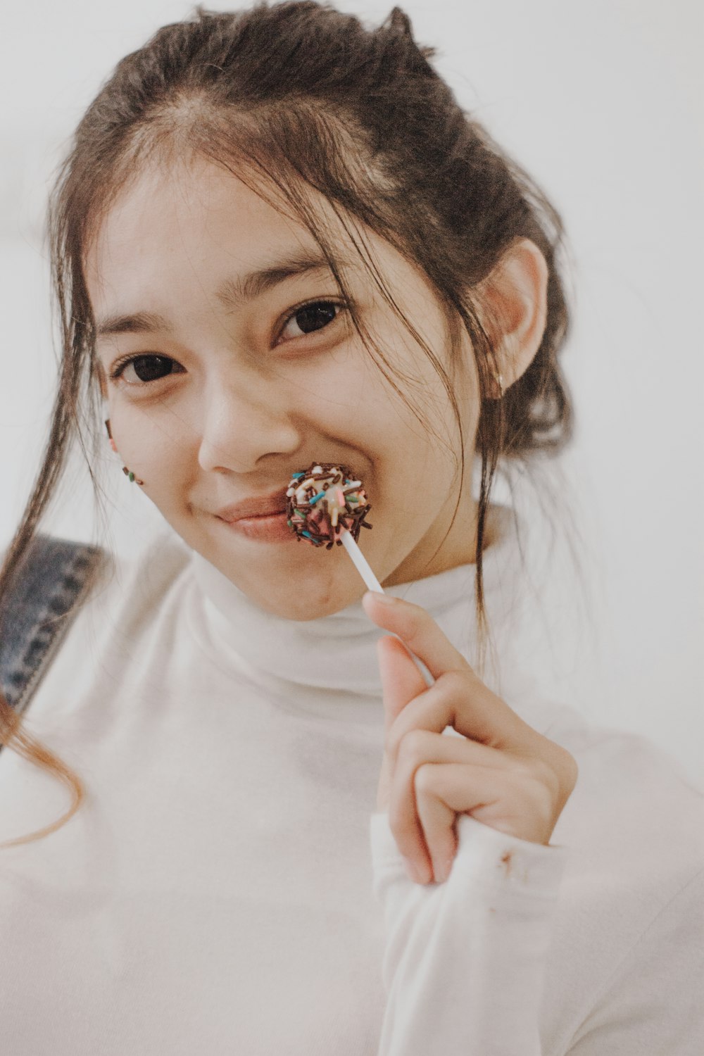 girl in white crew neck shirt holding brown and white lollipop