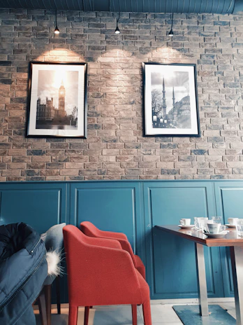 Warm, inviting photo of a Scandinavian-style café corner with matte forest green chairs and deep crimson cushions.