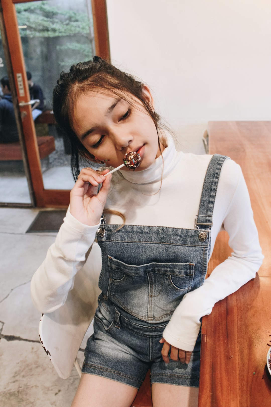 woman in white long sleeve shirt and blue denim dungaree eating