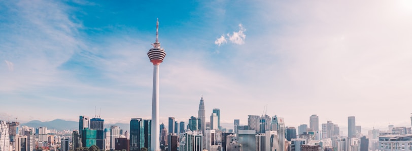 A city skyline featuring a prominent communication tower in the foreground, surrounded by modern skyscrapers under a clear blue sky.