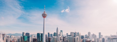 A city skyline featuring a prominent communication tower in the foreground, surrounded by modern skyscrapers under a clear blue sky.