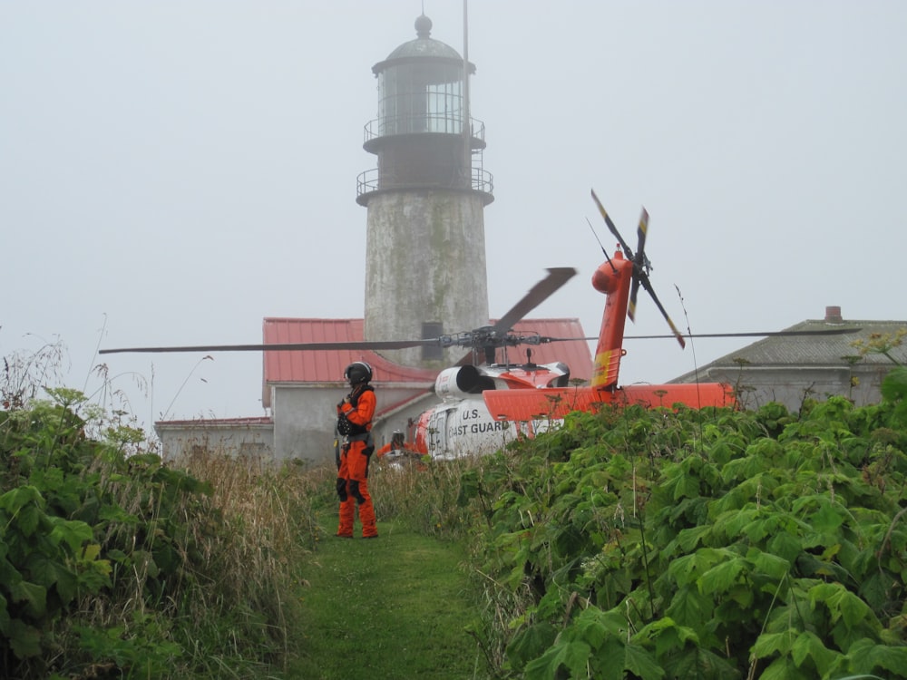 man in white shirt and orange pants standing near white lighthouse during daytime