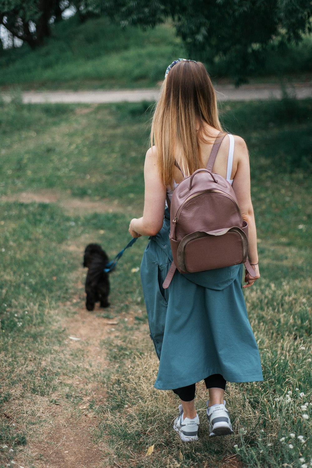 woman in blue dress carrying black dog on green grass field during daytime