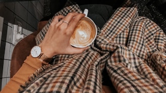 A hand wearing a classic watch, holding a cup of coffee in a cozy setting.