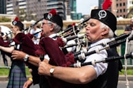 A piper tuning their bagpipes outdoors with a scenic backdrop.