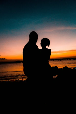 Wide-angle view of a couple embracing as the sun dips below the horizon on a calm sea.