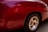 A close-up view of a vintage car's rear quarter panel in a glossy red finish. The wheel features a chrome rim and thick tire with visible tread pattern. The reflective surface of the car body highlights the curves and contours.