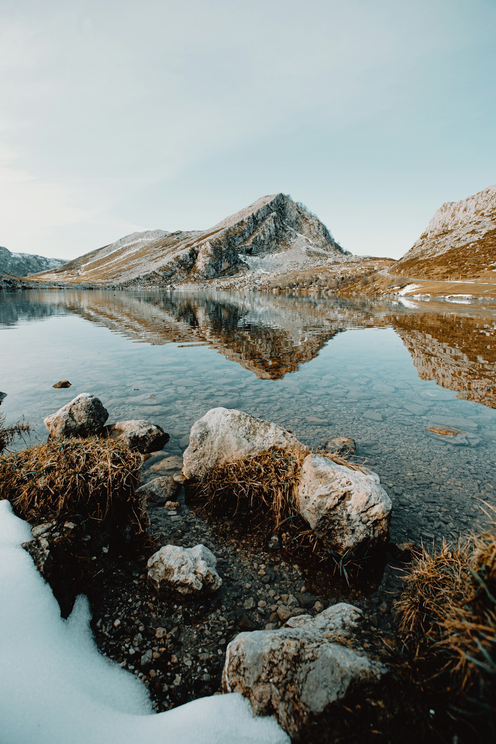 brown rocky mountain beside lake under blue sky during daytime